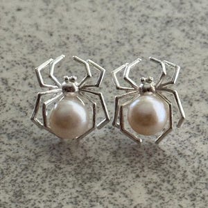 May include: A pair of silver spider earrings with a pearl in the center of each spider.