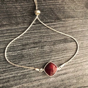 Peut inclure: Un bracelet en chaîne argent avec un pendentif en pierre rouge. Le bracelet est doté d'un fermoir coulissant réglable.