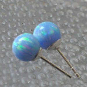 May include: A pair of blue opal stud earrings with silver posts. The opals have a light blue base with iridescent green and pink flashes.