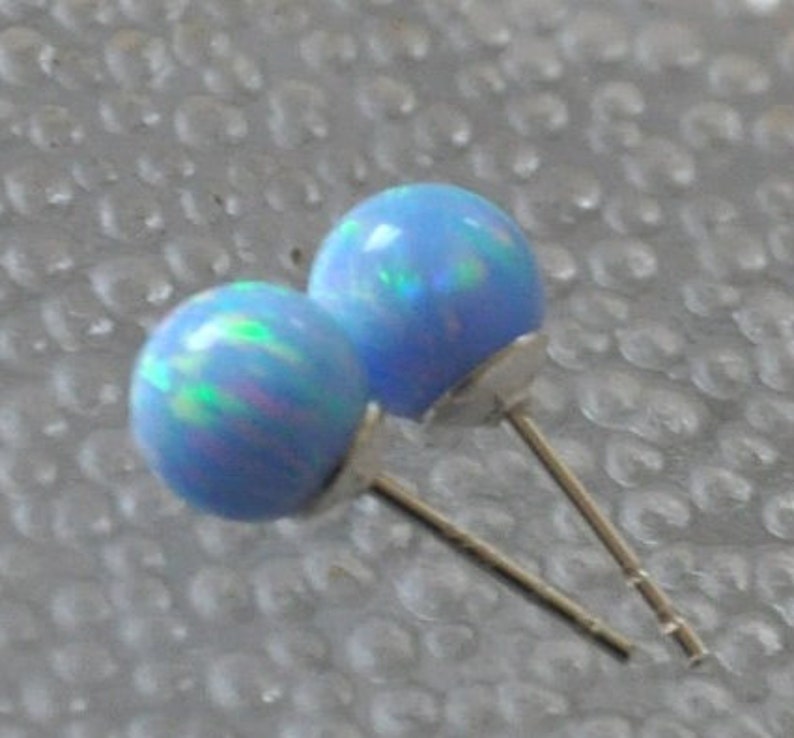 May include: A pair of blue opal stud earrings with silver posts. The opals have a light blue base with iridescent green and pink flashes.