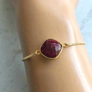 May include: A gold chain bracelet with a large, red, faceted gemstone pendant.