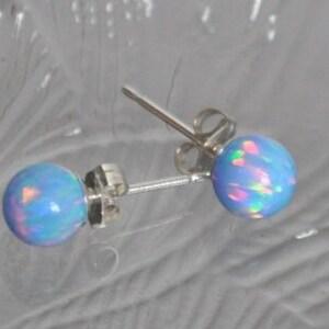 May include: A pair of silver stud earrings with light blue opal stones. The opals have a rainbow iridescent sheen.