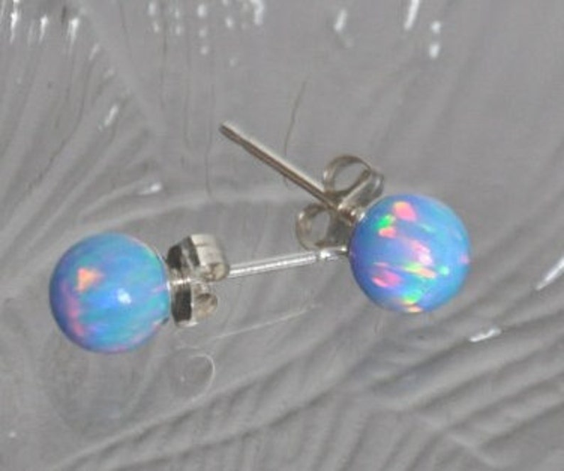 May include: A pair of silver stud earrings with light blue opal stones. The opals have a rainbow iridescent sheen.