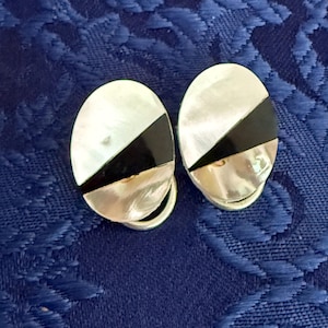 May include: A pair of oval earrings with a silver backing. Each earring has a diagonal black stripe between a white and silver section. The earrings are set against a blue background.