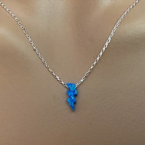 May include: A silver chain necklace with a blue lightning bolt pendant. The pendant has a textured, opal-like appearance. The necklace is displayed against a neutral background.