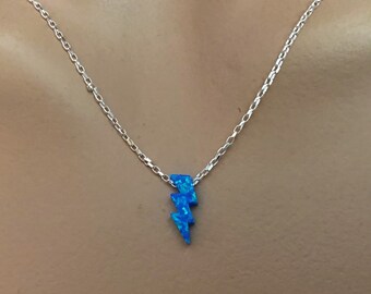May include: A silver chain necklace with a blue lightning bolt pendant. The pendant has a textured, opal-like appearance. The necklace is displayed against a neutral background.