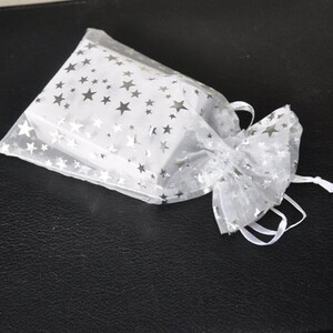 May include: A white organza gift bag with silver stars printed on it. The bag is tied with a white ribbon.