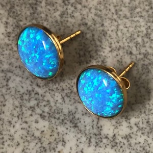 May include: A pair of gold stud earrings with blue opal stones. The stones have a sparkly, iridescent finish.