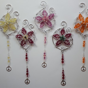 May include: Five decorative floral ornaments with wire frames and colourful beaded petals. Each flower has a different colour scheme, including yellow, pink, and orange. They feature dangling beaded strands and peace sign charms, ideal for home decor.