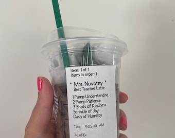 May include: A clear plastic cup with a green straw, filled with ice and a brown beverage. The cup has a white label with the text "Mrs. Novotny Best Teacher Latte" and a list of ingredients: "1 Pump Understanding, 2 Pump Patience, 3 Shots of Kindness, Sprinkle of Joy, Dash of Humility". The label also includes the time "9:05:00 AM" and the text ">CAFE<".