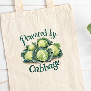 May include: A white canvas tote bag with green text that reads "Powered by Cabbage" and a green illustration of a bunch of cabbages.