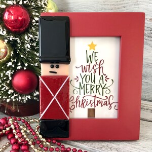 May include: A red frame with a glass mosaic of a toy soldier and a white background with the text "We wish you a Merry Christmas".
