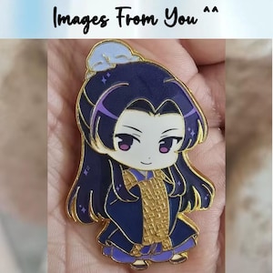 May include: A gold-colored enamel pin featuring a chibi-style character with long dark blue hair and purple eyes. The character wears a dark blue robe with gold accents and a small hat. The text "Images From You ^^" is at the top.