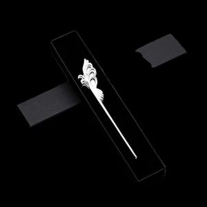 May include: A black rectangular box with a white decorative hair stick. The hair stick features an ornate, stylized floral design at the top and a long, slender stem. The background is solid black.