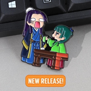 May include: Enamel pin featuring two anime-style characters in traditional clothing. One character is in blue and gold, the other in green. The pin includes a small brown table and the text "NEW RELEASE!" in an orange banner.