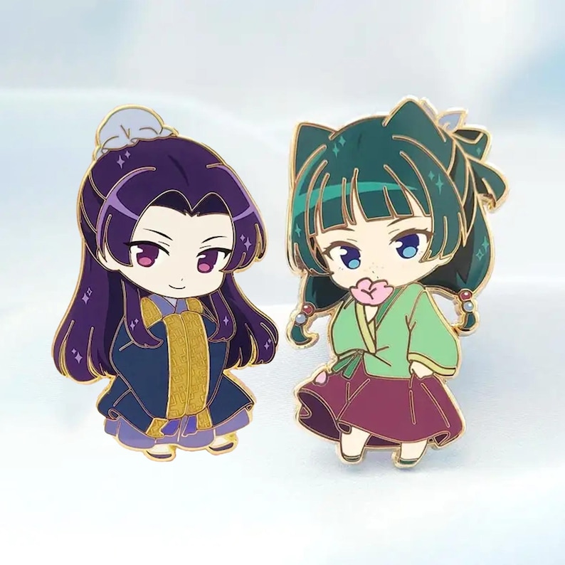 May include: Two enamel pins featuring anime-style characters. One has purple hair and a blue and gold outfit. The other has green hair, a green and maroon outfit, and holds a pink flower. Both pins have gold outlines and are set against a light blue background.