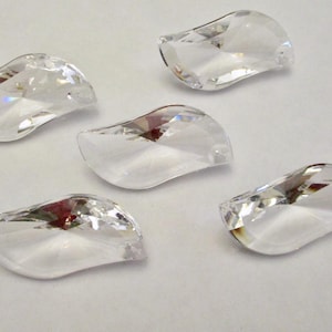 May include: Five clear, curved crystal pendants are scattered on a white surface. Each pendant has a rounded shape with a flat back and a pointed tip. The crystals reflect light, creating a sparkling effect.