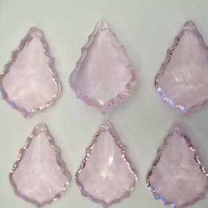 May include: Six light pink, teardrop-shaped crystal pendants with faceted surfaces and scalloped edges. The crystals are arranged in two rows of three against a white background. These decorative crystals are suitable for jewelry making or craft projects.