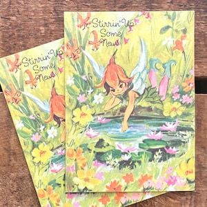 Peut inclure: Deux cartes postales vintage avec une illustration de fée. La fée est verte et orange avec des ailes et elle atteint un étang avec des nénuphars. Le texte sur la carte postale est "Stirrin' Up Some News".