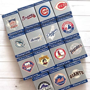 May include: A collection of fourteen grey rectangular boxes of Collector's Edition playing cards, each featuring a unique Major League Baseball team logo, including the Braves, Cubs, Reds, Dodgers, Expos, Marlins, Astros, Pirates, Cardinals, Padres, Phillies, Rockies, Mets, and Giants.