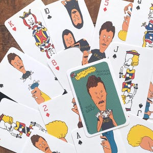 May include: A deck of playing cards featuring cartoon characters. The cards have various face values and suits, with the characters replacing traditional card figures. A promotional card with the text "THIS SUCKS!" is also included.