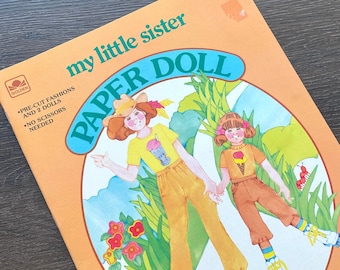 May include: A Golden Book paper doll set featuring two sisters with pre-cut fashions. The cover features an illustration of the sisters wearing summer outfits and roller skates. The title of the book is "My Little Sister Paper Doll".