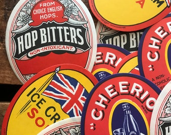 May include: A collection of vintage, round, paper coasters with colorful designs and text. The coasters feature various designs, including a Union Jack flag, a hops design, and a cherry design. The text on the coasters includes "Hop Bitters Non-Intoxicant", "Ice Cream Soda", "Cheerios", and "A Non-Alcoholic Beverage".