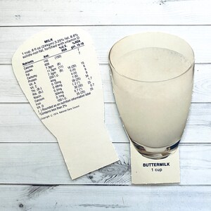 May include: A white card with nutritional information for a cup of milk. The card is shaped like a glass of milk. The text on the card reads "MILK 1 cup, 8 fl oz (244gm) 3.25% fat. 8.6% solids-not-fat, fortified with vitamin D %U.S. %RDA Nutrients Amt. RDA girl, 15-18 Calories 145 (150) 7 Joules 609 7 Fat 7.9gm (8) 16 (20) 15 Carbohy 11.3gm (11) 5 (4) 6 Protein 7.3gm (8) 4 (4) 9 Vit. A 250 1.U. 7 (6) 9 Vit. C 4mg 28 (25) 34 Thi. (B) 0.10mg 1.2 (*) 1.7 Rib. (Ba) 0.48mg 30 (30) 25 Niacin 0.2mg 0.7 (*) 0.7 Calcium 304mg 25 (25) 25 Iron 0.1mg "Contains less than 2% ()Rounded as on nutrition information label Copyright 1974, National Dairy Council"  BUTTERMILK 1 cup