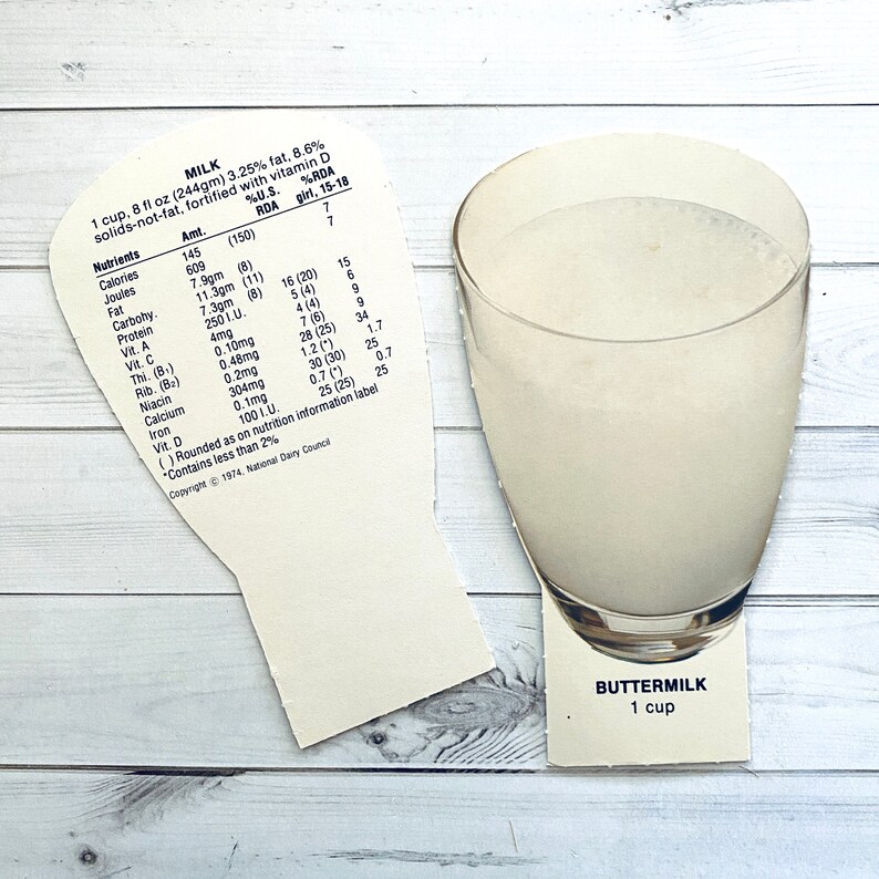 May include: A white card with nutritional information for a cup of milk. The card is shaped like a glass of milk. The text on the card reads "MILK 1 cup, 8 fl oz (244gm) 3.25% fat. 8.6% solids-not-fat, fortified with vitamin D %U.S. %RDA Nutrients Amt. RDA girl, 15-18 Calories 145 (150) 7 Joules 609 7 Fat 7.9gm (8) 16 (20) 15 Carbohy 11.3gm (11) 5 (4) 6 Protein 7.3gm (8) 4 (4) 9 Vit. A 250 1.U. 7 (6) 9 Vit. C 4mg 28 (25) 34 Thi. (B) 0.10mg 1.2 (*) 1.7 Rib. (Ba) 0.48mg 30 (30) 25 Niacin 0.2mg 0.7 (*) 0.7 Calcium 304mg 25 (25) 25 Iron 0.1mg "Contains less than 2% ()Rounded as on nutrition information label Copyright 1974, National Dairy Council"  BUTTERMILK 1 cup