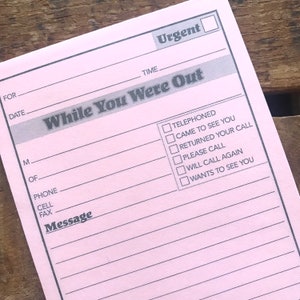 Puede incluir: Un bloc de notas rosa con las palabras "While You Were Out" impresas en negro. El bloc de notas tiene una lista de verificación con opciones para "Telephoned", "Came to See You", "Returned Your Call", "Please Call", "Will Call Again" y "Wants to See You". Hay un espacio para la fecha, la hora y un mensaje.