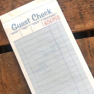 Puede incluir: Un cheque de restaurante blanco con líneas azules y las palabras "Guest Check" impresas en azul. El número de cheque "606950" está impreso en rojo.