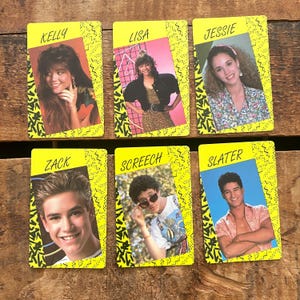 May include: Six vintage trading cards featuring characters named Kelly, Lisa, Jessie, Zack, Screech, and Slater. Each card has a yellow border with a black and white zigzag design. The cards display headshots of the characters.