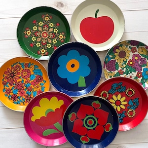 May include: A collection of vintage metal trays with colorful floral and fruit designs. The trays feature a variety of colors, including red, green, blue, yellow, and pink. Each tray has a unique pattern, such as an apple, a large flower, or a floral arrangement.