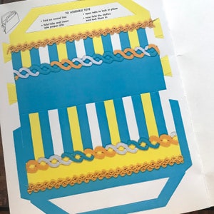 May include: A blue and yellow striped tote bag with a white and yellow striped border. The tote bag has a scalloped edge and a fold-over flap with tabs to lock in place. The instructions for assembling the tote bag are printed on the white background.