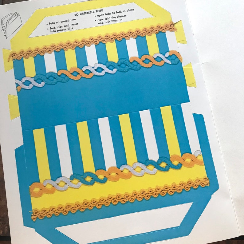 May include: A blue and yellow striped tote bag with a white and yellow striped border. The tote bag has a scalloped edge and a fold-over flap with tabs to lock in place. The instructions for assembling the tote bag are printed on the white background.