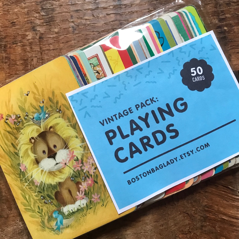 Może przedstawiać: Winietkowy zestaw 50 kart do gry z niebieskim tłem i białym tekstem. Tekst brzmi "Vintage Pack: Playing Cards" i "bostonbaglady.etsy.com". Prz&oacute;d talii kart przedstawia kresk&oacute;wkowego lwa z ż&oacute;łtą grzywą i brązowym futrem.
