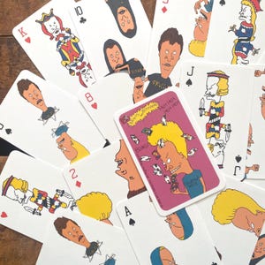 以下が含まれることがあります： 漫画のキャラクターが描かれたトランプ。各カードには異なる数字とマークが表示されています。1枚のカードには「BEAVIS AND BUTTHEAD」と「BOING！」の文字が印刷されています。