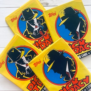 Puede incluir: Varios paquetes de cromos de la película "Dick Tracy" de Topps. Cada paquete presenta un fondo amarillo con una imagen circular de Dick Tracy con sombrero y un borde azul. El texto "Dick Tracy Movie Cards" es visible.