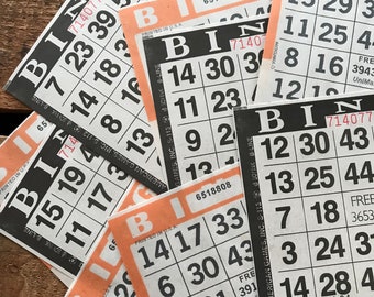 May include: Close-up of several bingo cards with numbers and the word "Bingo" printed on them. The cards are orange and black with white numbers. The cards are arranged in a random order.