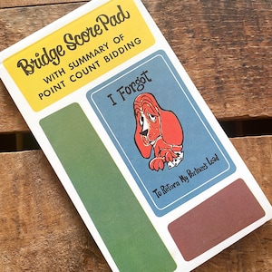 May include: A green, blue, and yellow bridge score pad with the text "Bridge Score Pad" and "I Forgot" on the front. The pad has a cartoon illustration of a bloodhound dog with the text "To Return My Partner's Lead".