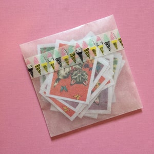May include: A clear plastic bag filled with a stack of colorful paper cards featuring a cat illustration. The bag is sealed with a decorative tape featuring a repeating pattern of ice cream cones.