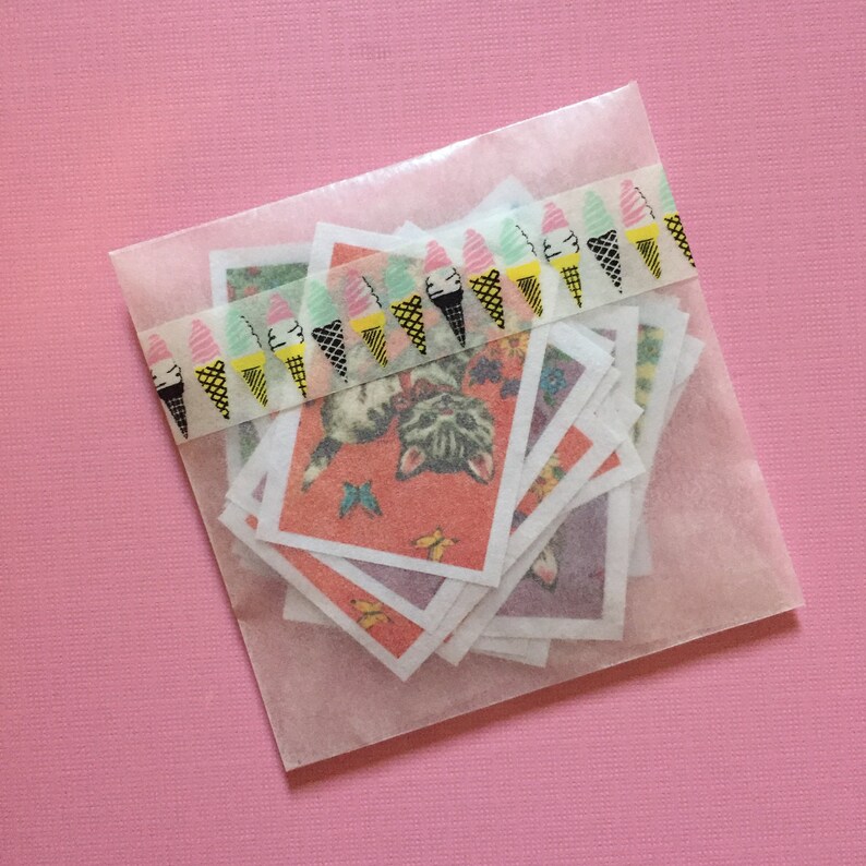 May include: A clear plastic bag filled with a stack of colorful paper cards featuring a cat illustration. The bag is sealed with a decorative tape featuring a repeating pattern of ice cream cones.