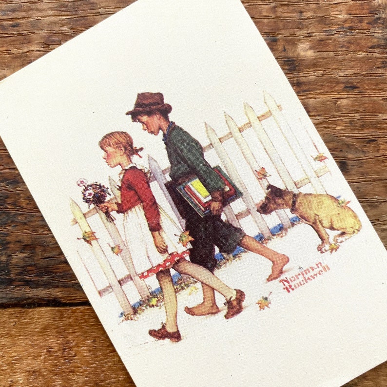 May include: A vintage print featuring a boy and girl walking past a white picket fence with a dog. The boy carries books, and the girl holds flowers. The artwork is signed "Norman Rockwell". The scene is set in autumn with falling leaves.