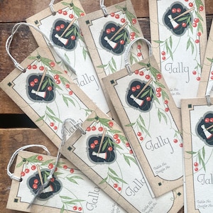May include: A pile of vintage-style tags with a decorative design. Each tag features a central illustration of a black and white object with a wooden handle, surrounded by red cherries and green leaves. The word "Tally" is printed on each tag.
