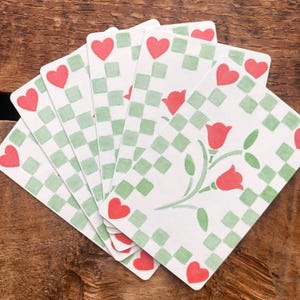 以下が含まれることがあります： 水彩デザインのトランプ。各カードは、緑のチェック柄と赤いハートのシンボルが付いた白い背景が特徴です。一部のカードには赤いチューリップのイラストが表示されています。