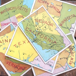 May include: A collection of vintage-style rectangular cards featuring colorful illustrated maps of various U.S. states including California, Nevada, Texas, Massachusetts, and New Jersey. Each card displays state names in red text with black city labels.