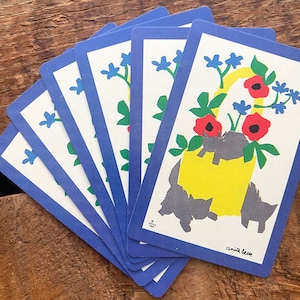 Puede incluir: Un juego de seis cartas con un borde azul y un dise&ntilde;o floral. Las cartas presentan un cubo amarillo con flores rojas y gatos negros. El texto en la tarjeta dice "Anita Beck".