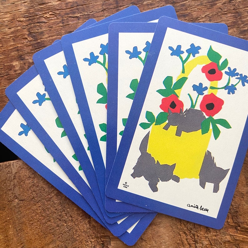 Puede incluir: Un juego de seis cartas con un borde azul y un dise&ntilde;o floral. Las cartas presentan un cubo amarillo con flores rojas y gatos negros. El texto en la tarjeta dice "Anita Beck".