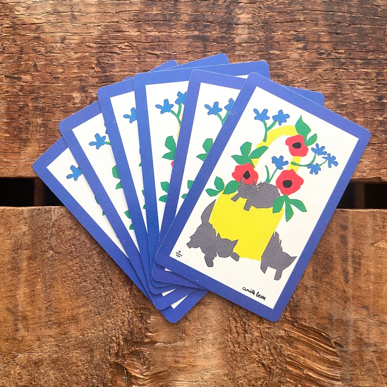 Puede incluir: Un juego de seis cartas de juego azules con un dise&ntilde;o floral y gatos negros. Las cartas presentan una jarra amarilla con flores rojas y hojas verdes. El texto en la carta dice "amia keen".