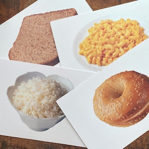 Puede incluir: Cuatro tarjetas blancas con diferentes alimentos en ellas. La tarjeta superior izquierda muestra una rebanada de pan integral. La tarjeta superior derecha muestra un tazón de macarrones con queso. La tarjeta inferior izquierda muestra un tazón de arroz blanco. La tarjeta inferior derecha muestra un bagel con semillas de sésamo.